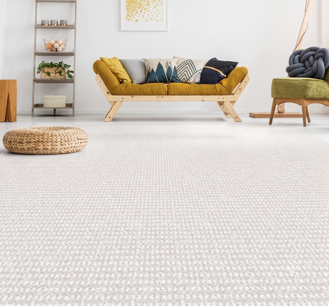 Light textured carpet remnant covering living room floor with mustard sofa and woven pouf, styled for a cozy modern space