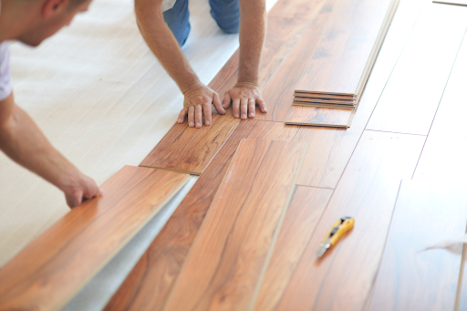 Two flooring contractors in Colorado Springs installing hardwood floors in a living room during a home renovation.